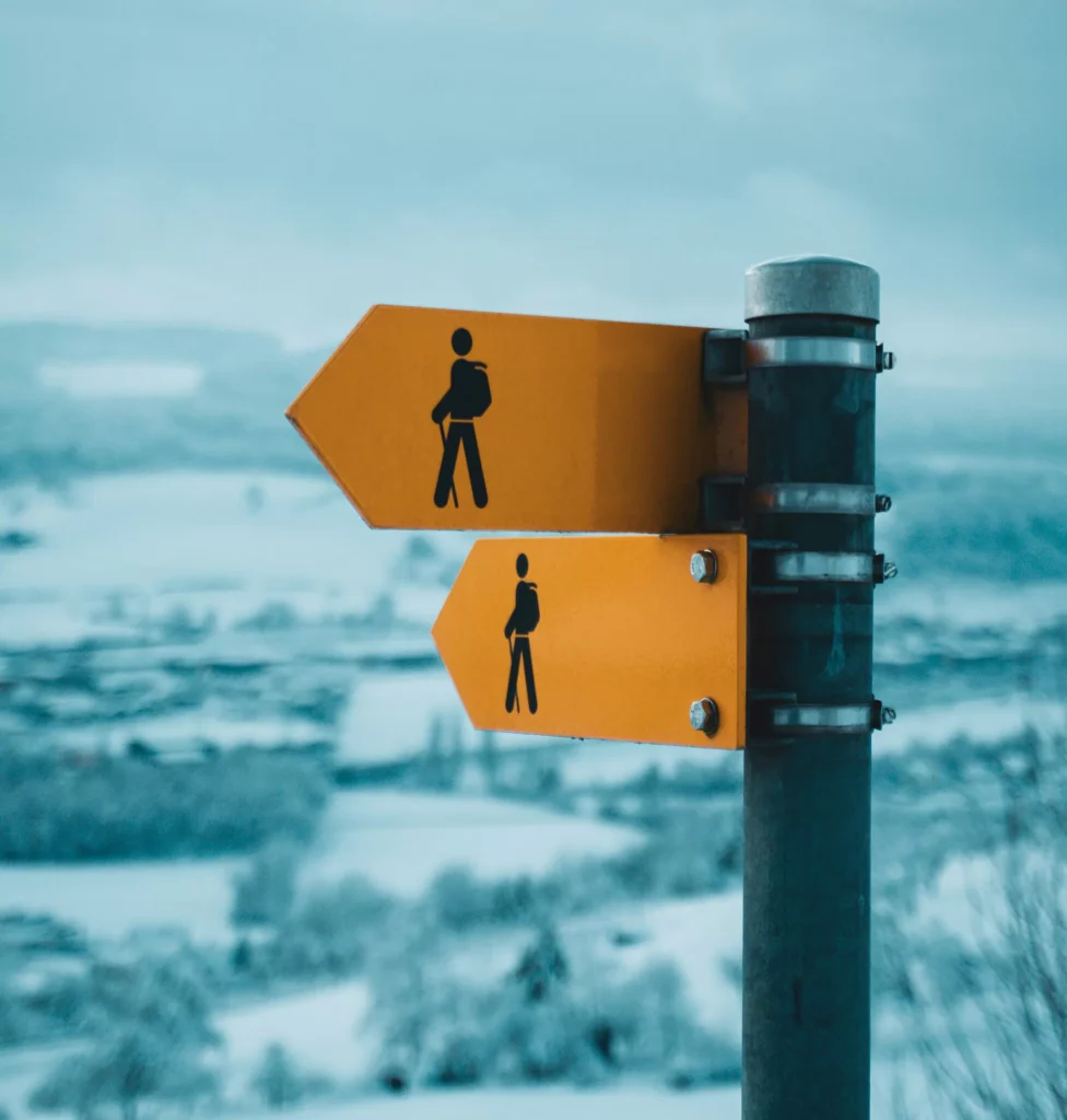 Yellow hiking trail signs pointing the way on a post above a snowy valley